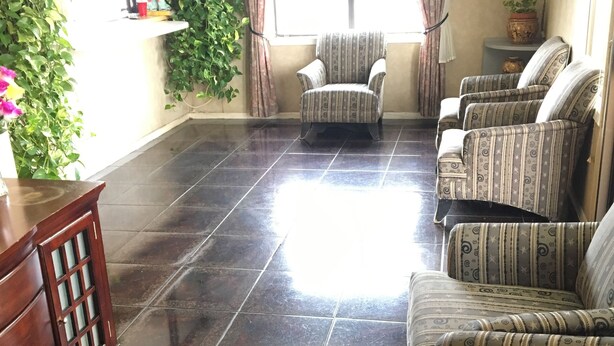 A spacious living area with a tiled floor, a sofa set, a wooden cabinet, and a large window with curtains. - Inn At Mexia (Mexia)