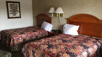 A hotel room with two beds, each with a patterned quilt, a wooden headboard, bedside lamps, and a framed picture on the wall.