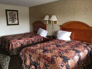 A hotel room with two beds, each with a patterned quilt, a wooden headboard, bedside lamps, and a framed picture on the wall.