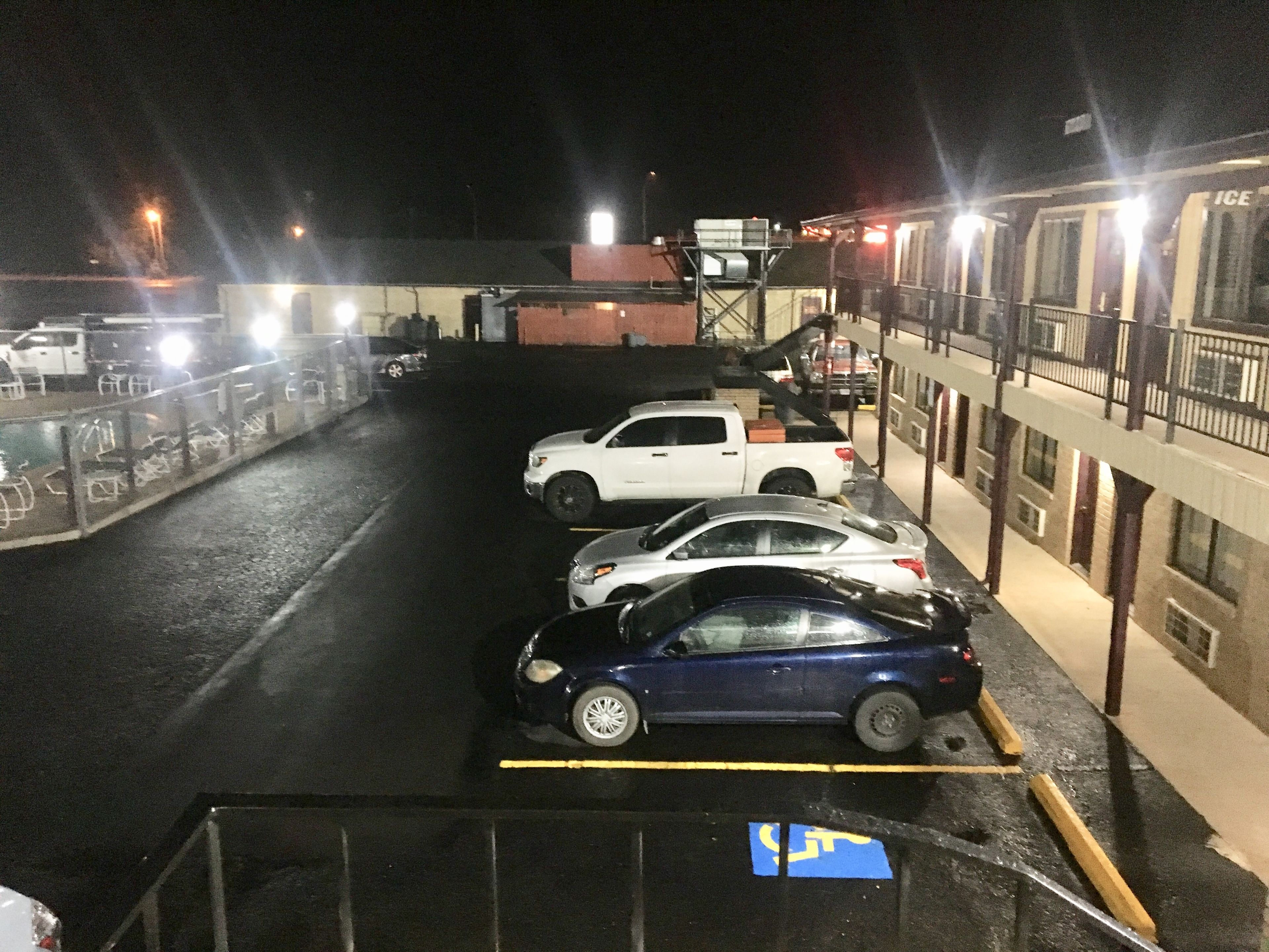 Een parkeerplaats 's nachts met verschillende auto's geparkeerd op aangegeven plaatsen, waaronder een parkeerplaats voor gehandicapten.