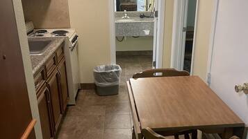 A compact kitchen with a dining table and chairs, a trash bin, and a view into the adjacent bathroom.