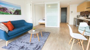 Una sala de estar moderna con un sofá azul, una mesita redonda con una planta y una mesa de comedor de vidrio con sillas.