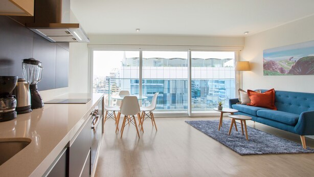 Una cocina moderna con comedor, un sofá azul y un ventanal con vistas a la ciudad.