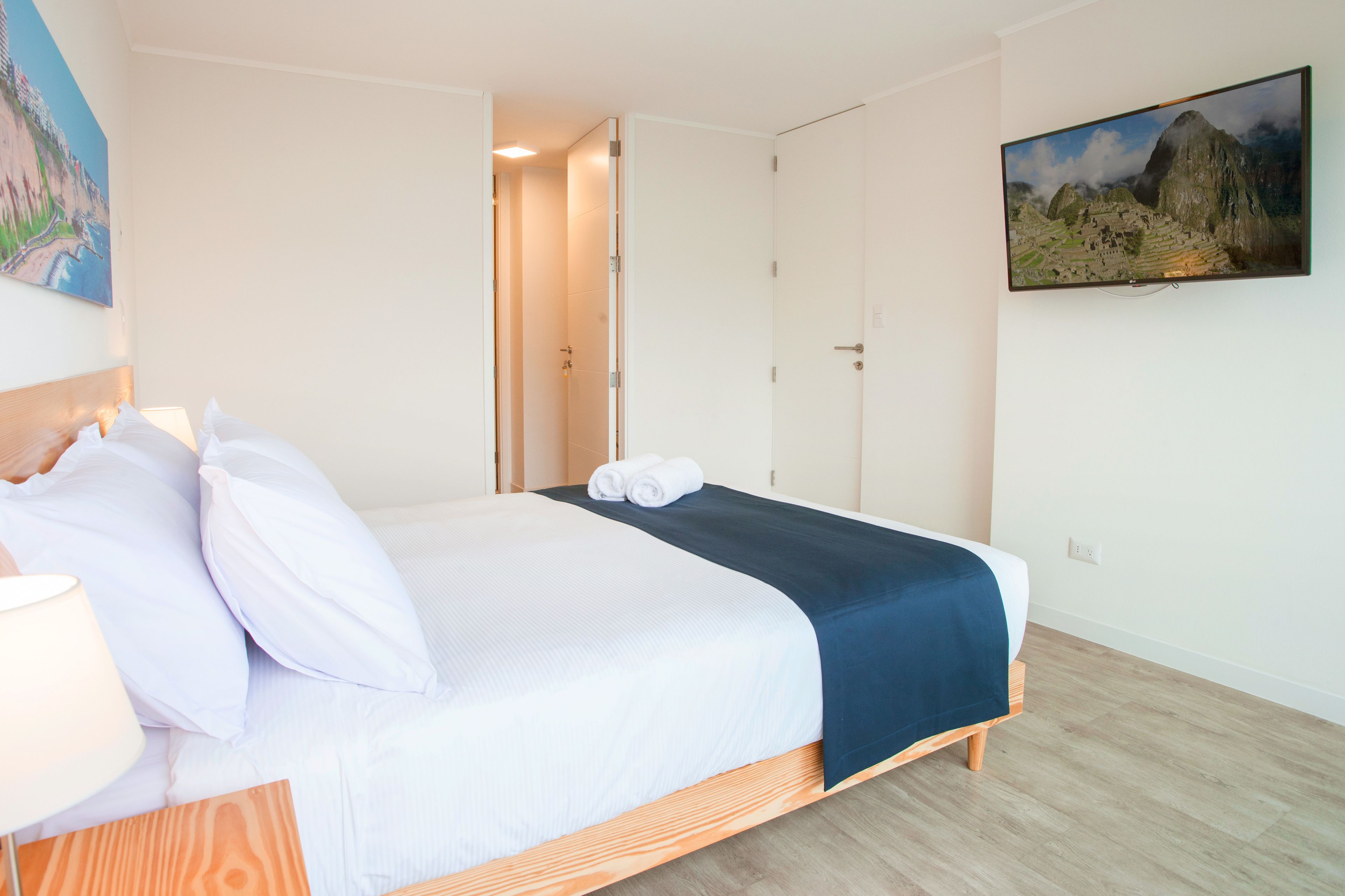 A hotel room with a bed, a painting on the wall, and a television displaying a landscape.
