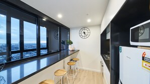 Uma cozinha moderna com grandes janelas, bancada preta, banquetas de madeira, relógio e geladeira.