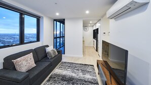 Sala de estar moderna com sofá, televisão e amplas janelas com vista para a cidade.