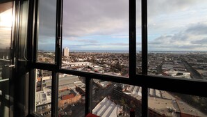 Vista urbana através de amplas janelas, com prédios e ruas à mostra.