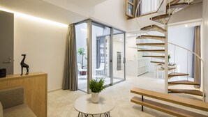 Una sala de estar moderna con una escalera en espiral, un ventanal que da a un área exterior y una mesita con una planta.