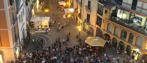 A crowded square with buildings on either side, a central open space, and a few people gathered around a table.