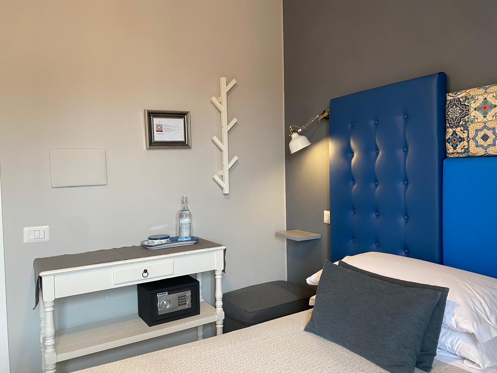 A bedroom with a bed, a desk, a chair, a lamp, and a wall-mounted shelf.