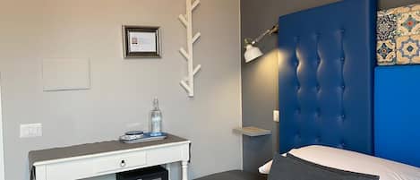 A bedroom with a bed, a desk, a chair, a lamp, and a wall-mounted shelf.