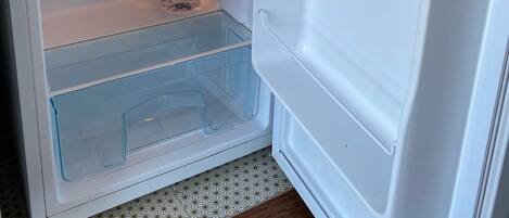 An open refrigerator with a bottle of water and a glass container on the shelf.