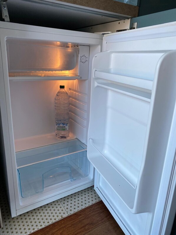 Un refrigerador abierto con una botella de agua y un recipiente de vidrio en el estante.