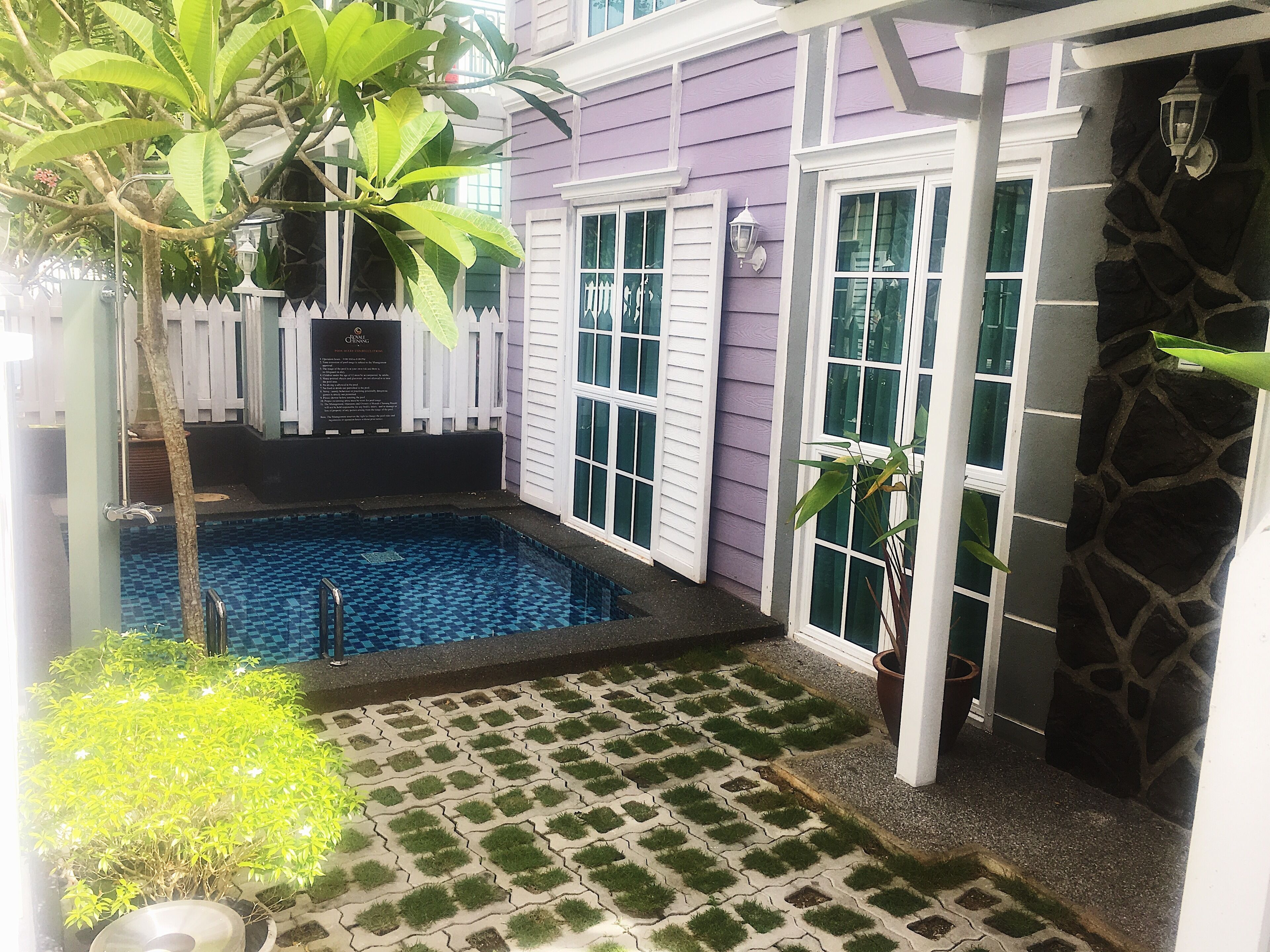 A pool area with a blue tiled floor, surrounded by a white fence, and a stone wall with a lantern.