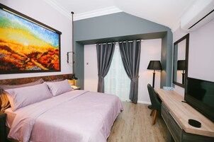 Ein Schlafzimmer mit einem Bett, einem Schreibtisch, einem Fernseher, einem Gemälde und einem Fenster mit Vorhängen.