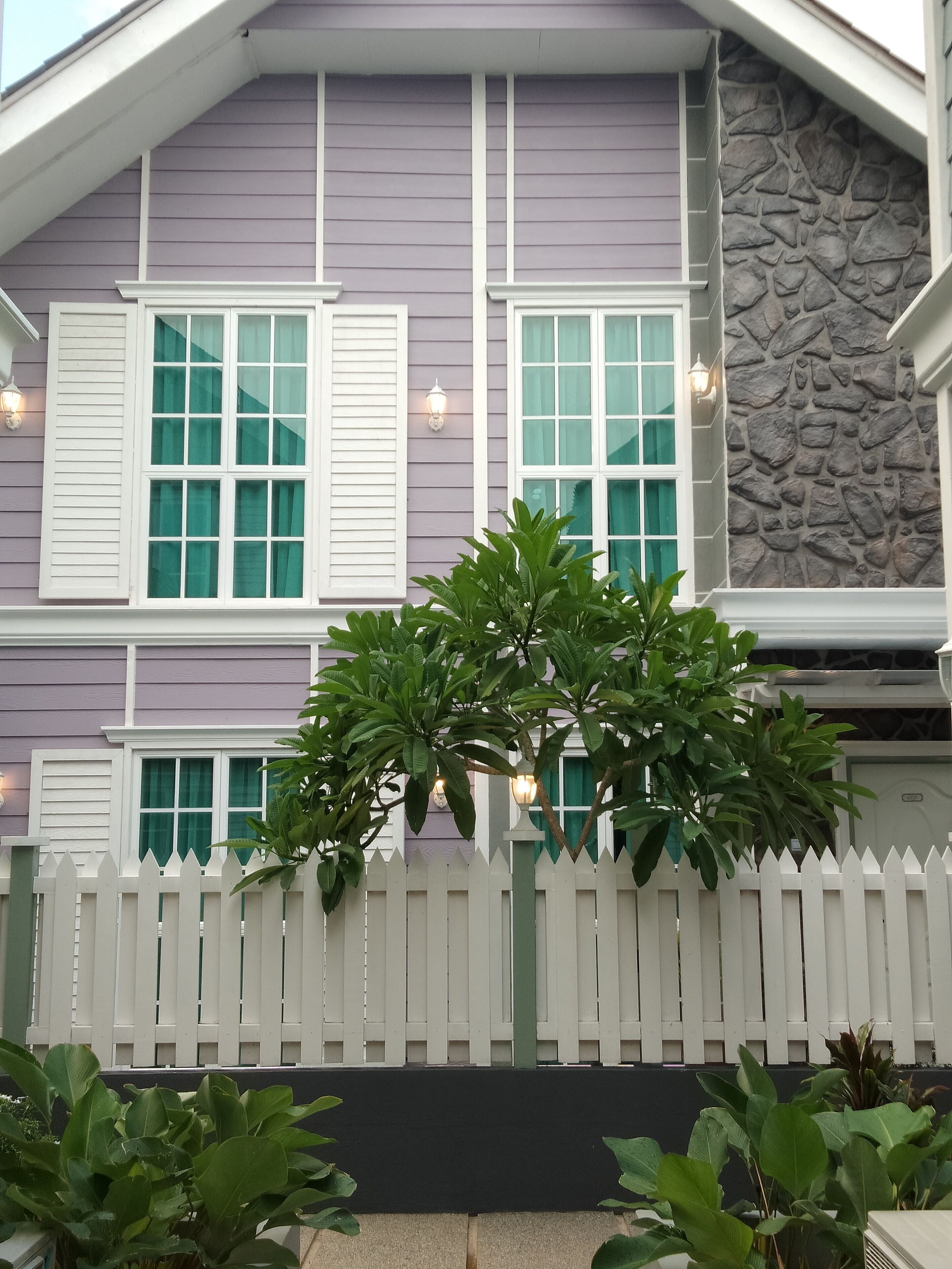 A house with a white picket fence, a stone wall, and a window with shutters.