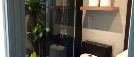 A modern bathroom with a glass-enclosed shower, a white toilet, and a shelf with white towels.