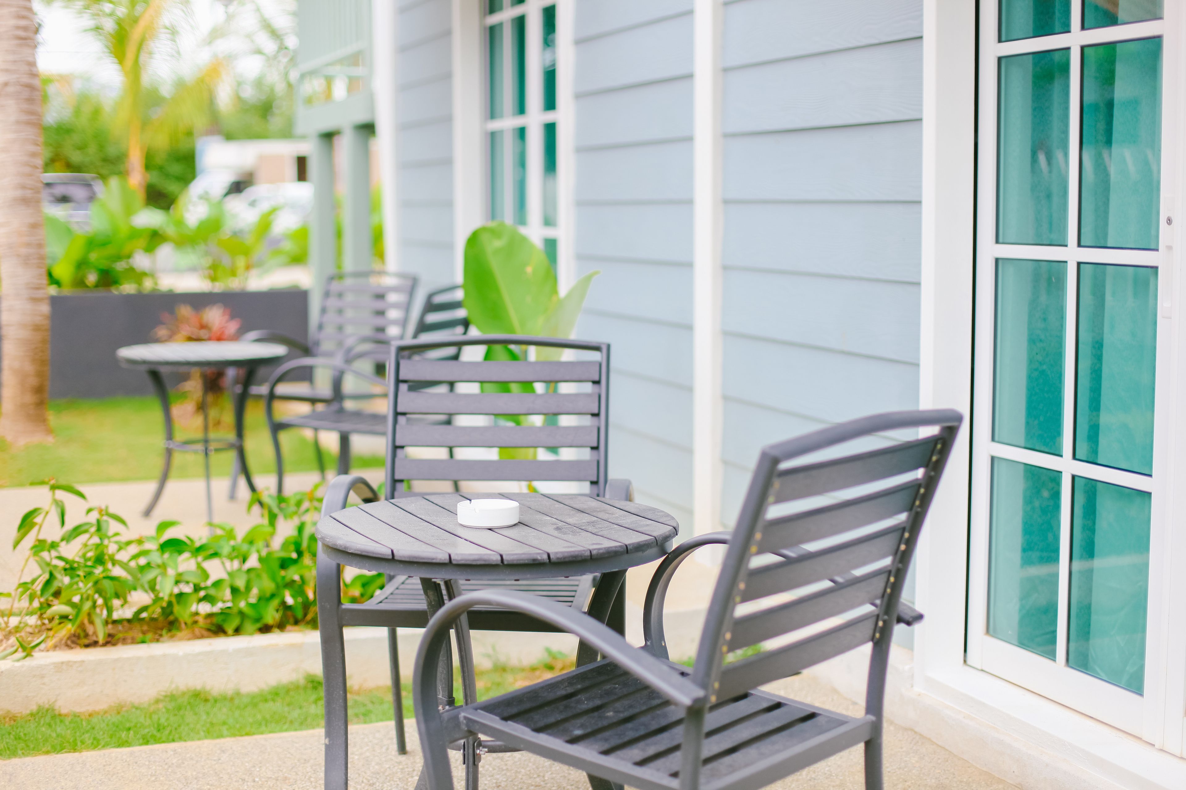 An outdoor seating area with a table and chairs, a small potted plant, and a window with a view of greenery.
