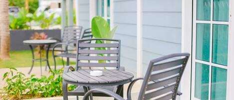 Un espace extérieur aménagé avec une table et des chaises, une petite plante en pot et une fenêtre donnant sur un paysage verdoyant.