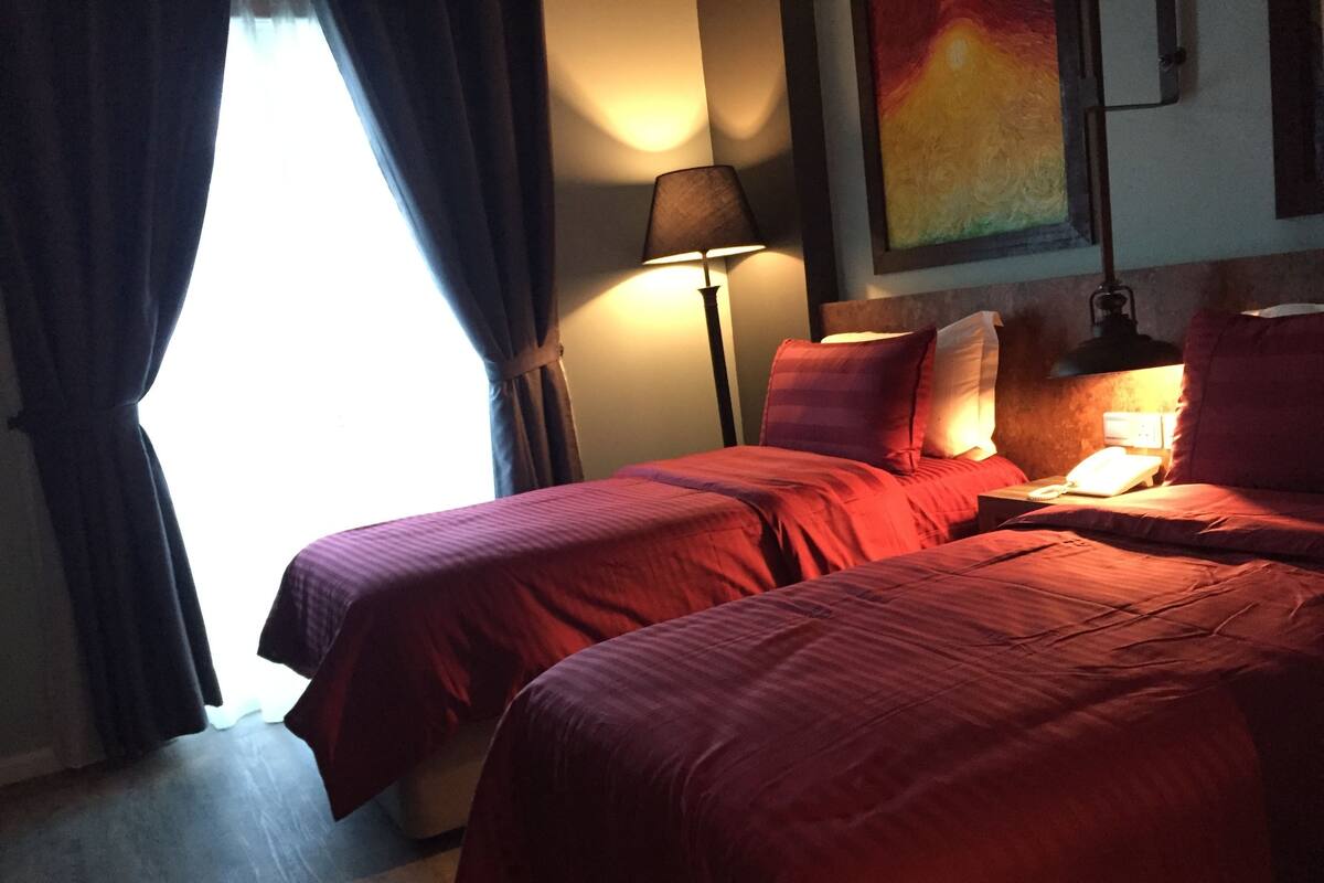 Ein Hotelzimmer mit zwei Betten, einer Lampe, einem Gemälde und einem Fenster mit Vorhängen.