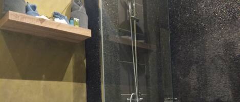 Un baño con inodoro, ducha con mampara de vidrio y estante con artículos de aseo.