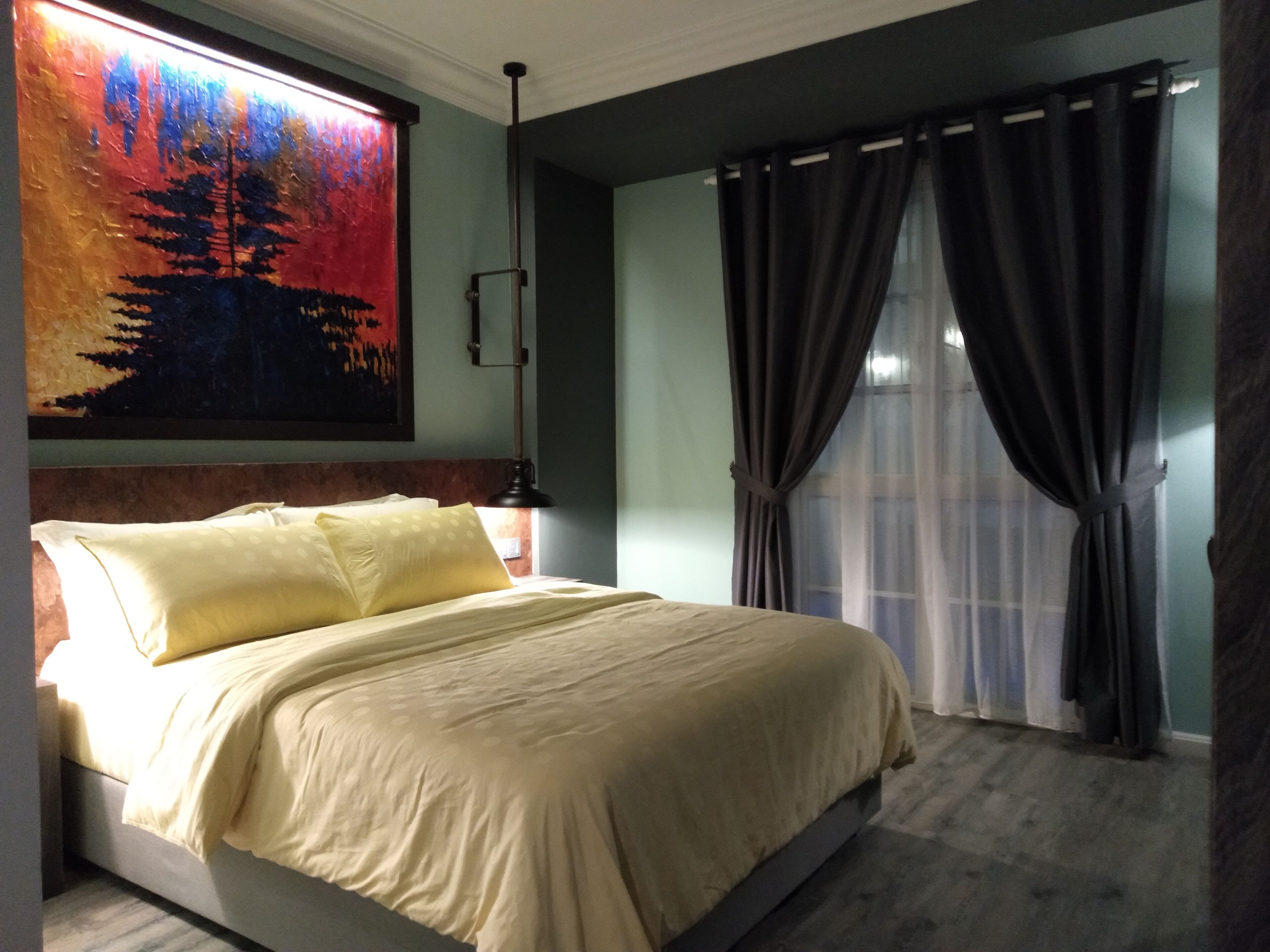 Een slaapkamer met een bed, een schilderij, een raam met gordijnen en een nachtkastje.
