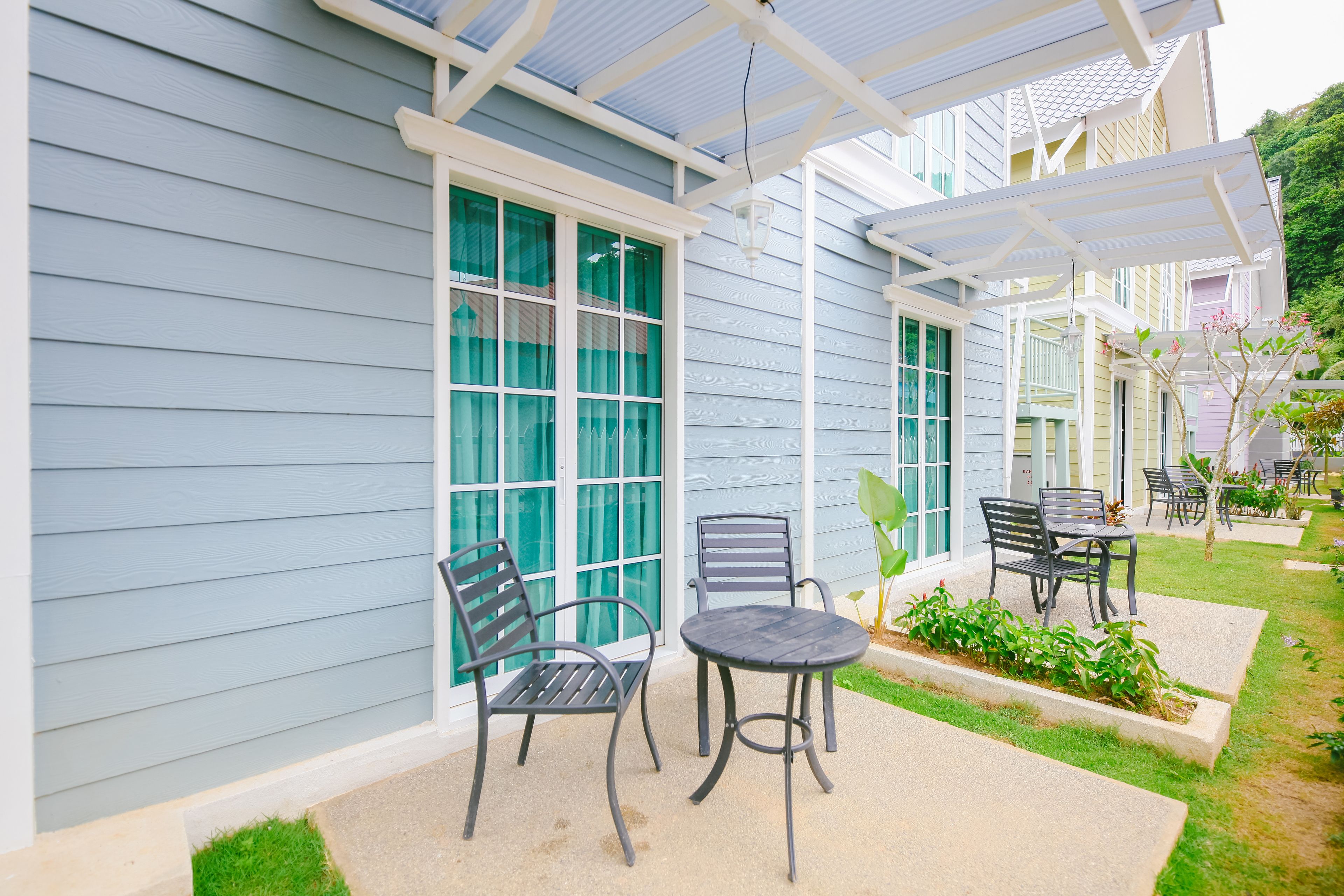 En overdækket terrasse med udendørs møbler, en pergola og udsigt til et hus med store vinduer.