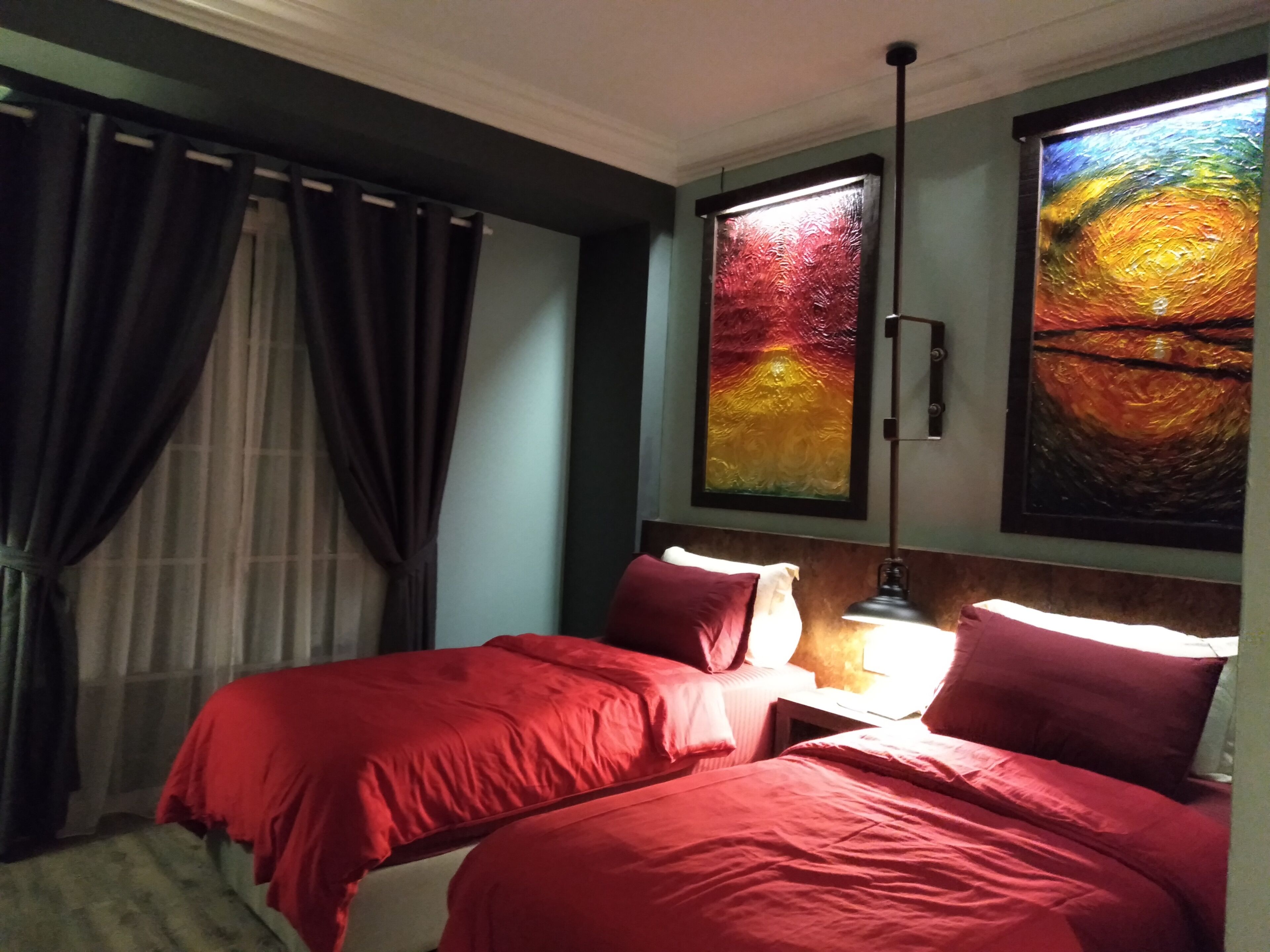 A hotel room with two beds, a nightstand, a lamp, and two paintings on the wall.