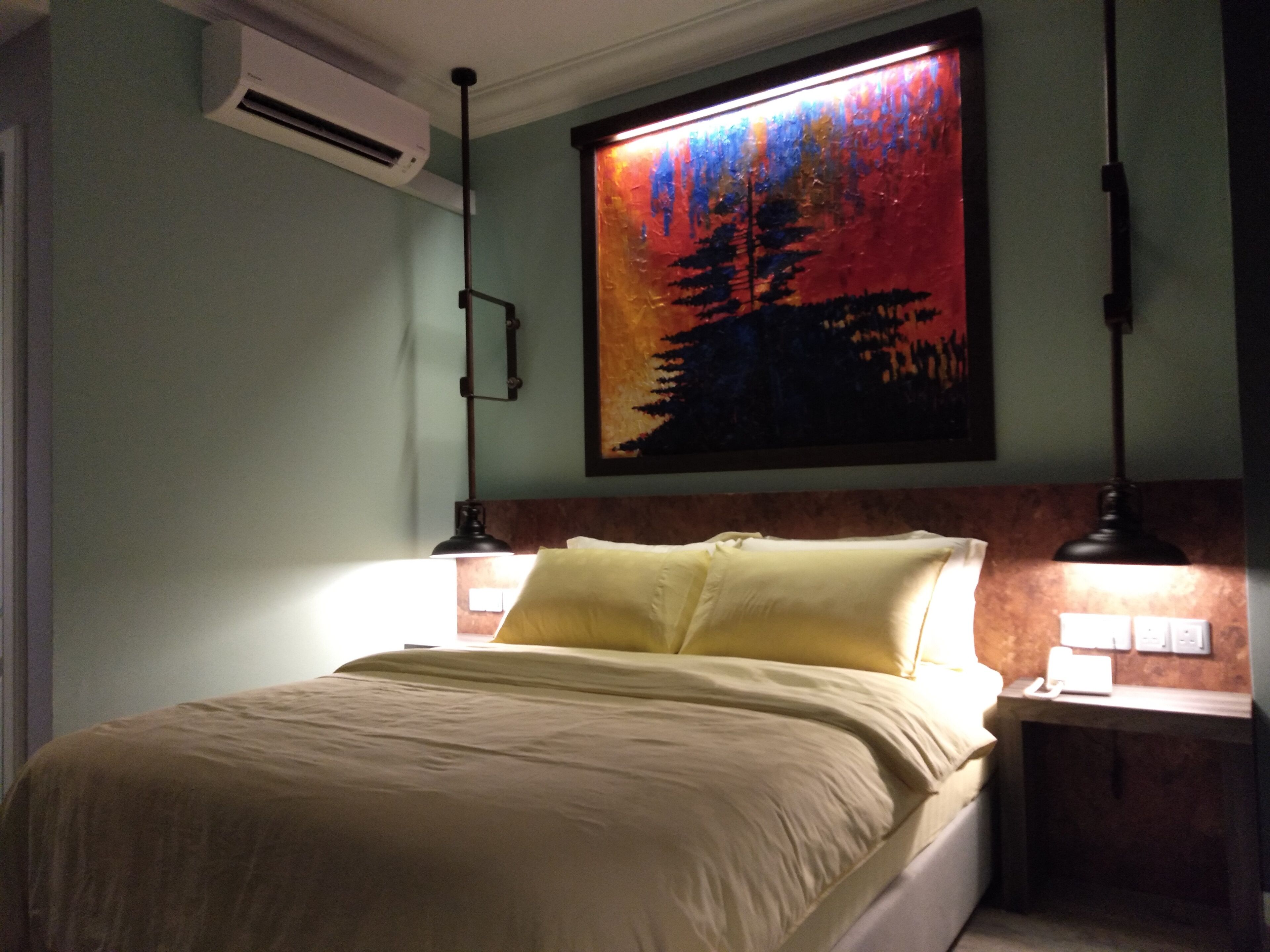 A bedroom with a bed, a nightstand, a wall-mounted air conditioner, and a painting above the bed.