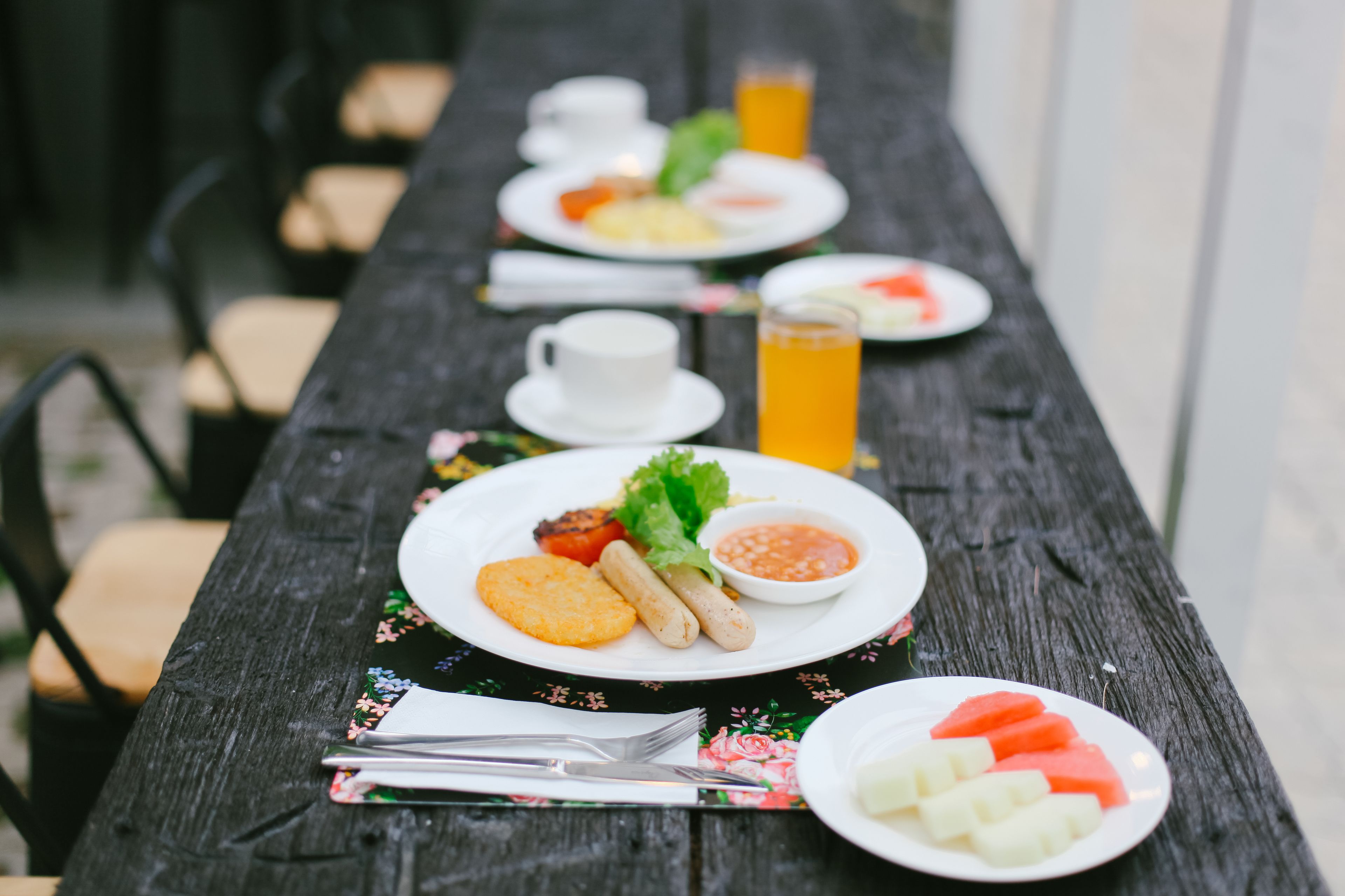 A wooden picnic table with plates of food, including watermelon, cheese, and a beverage.
