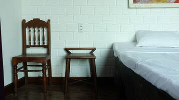 A room with a wooden chair, a small stool, and a bed with white bedding.