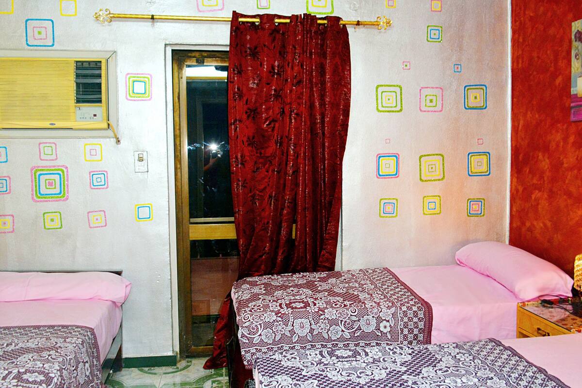 Une chambre avec deux lits, une fenêtre avec un rideau et un mur décoré de motifs carrés aux couleurs vives.