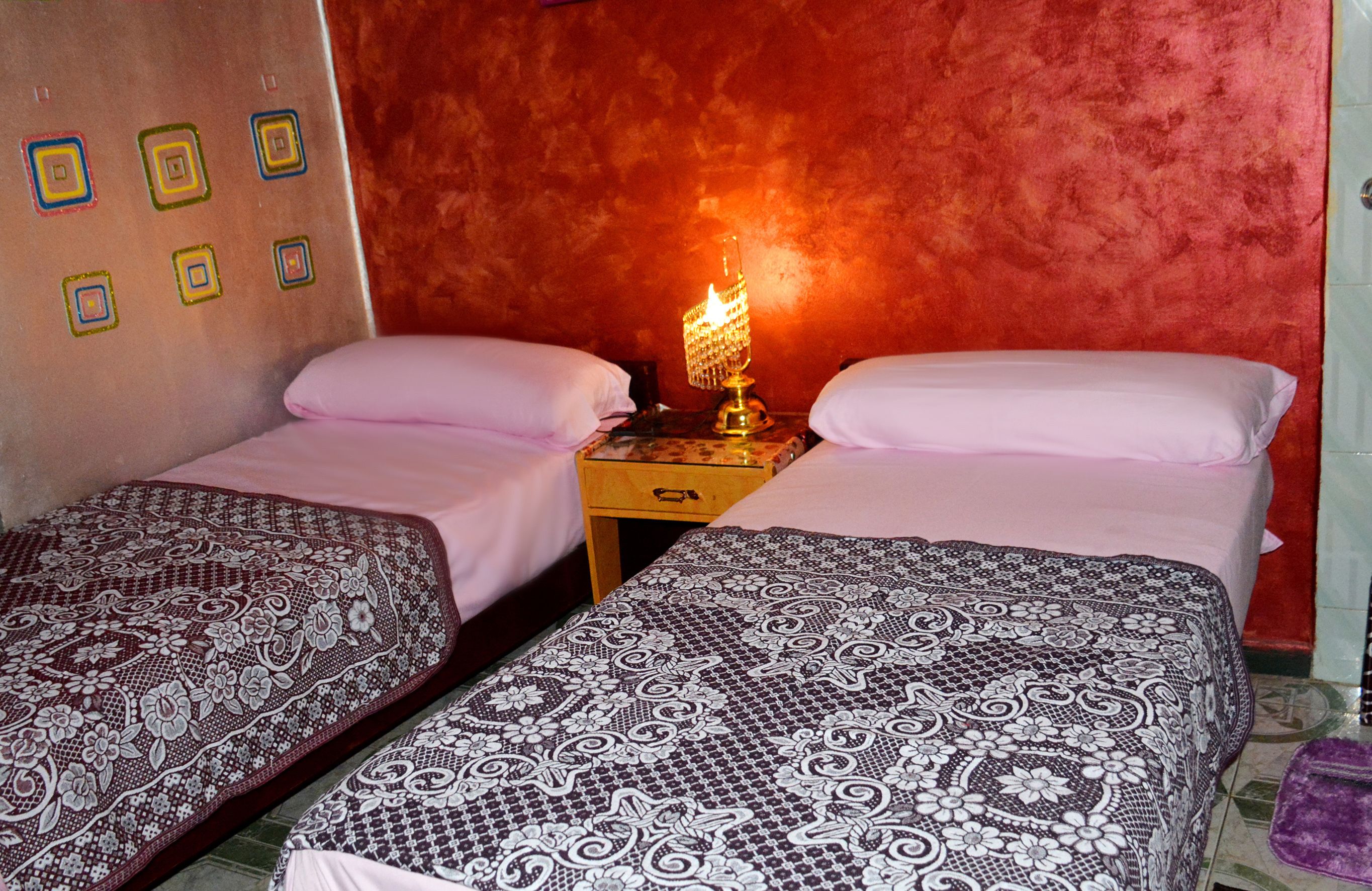 Een kamer met twee bedden, een nachtkastje met een lamp en een muur met vierkante patronen.