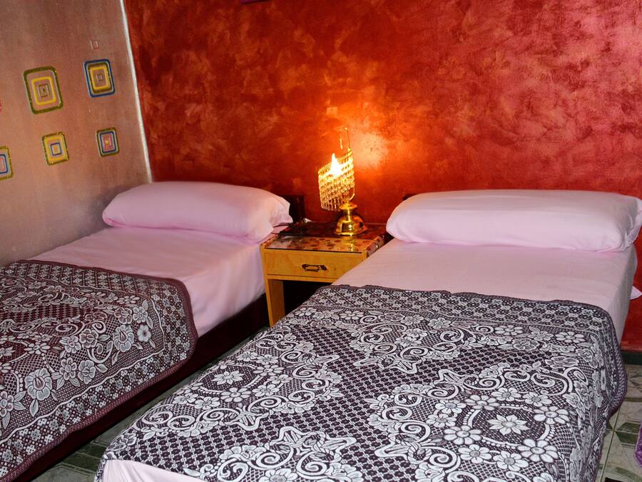 Een kamer met twee bedden, een nachtkastje met een lamp en een muur met vierkante patronen.