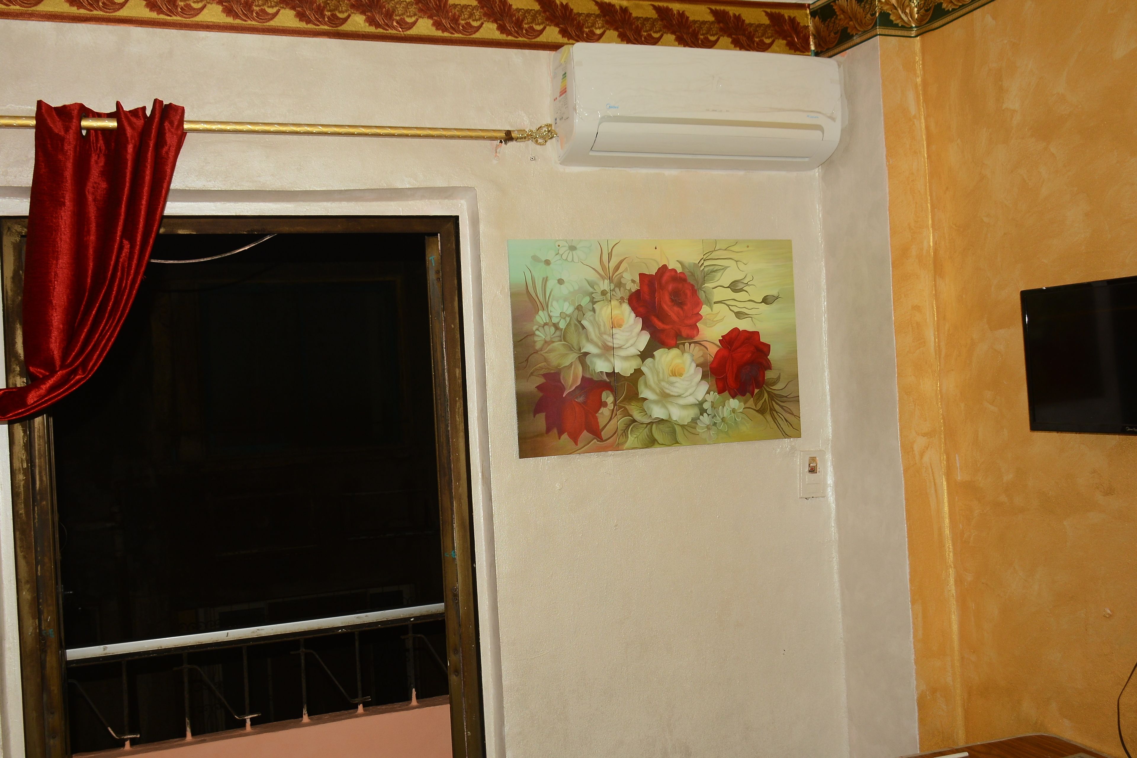 Una habitación con ventana, una cortina roja y un cuadro floral en la pared.