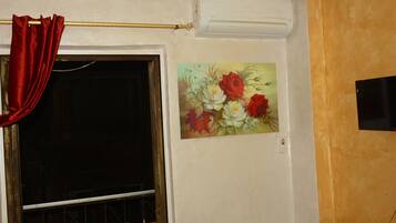 Una habitación con ventana, una cortina roja y un cuadro floral en la pared.