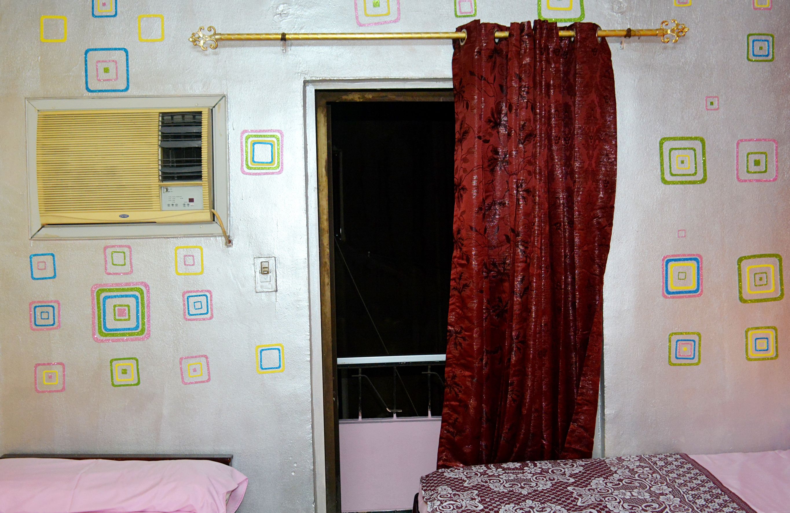 A room with a bed, a window with a curtain, and a wall decorated with colorful square patterns.