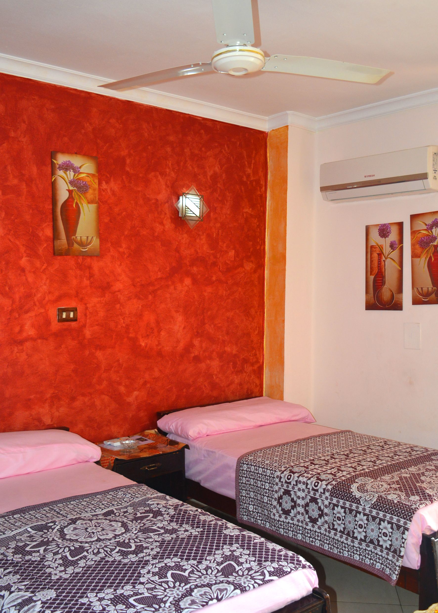 Habitación de hotel con dos camas, ventilador de techo y obras de arte en las paredes.