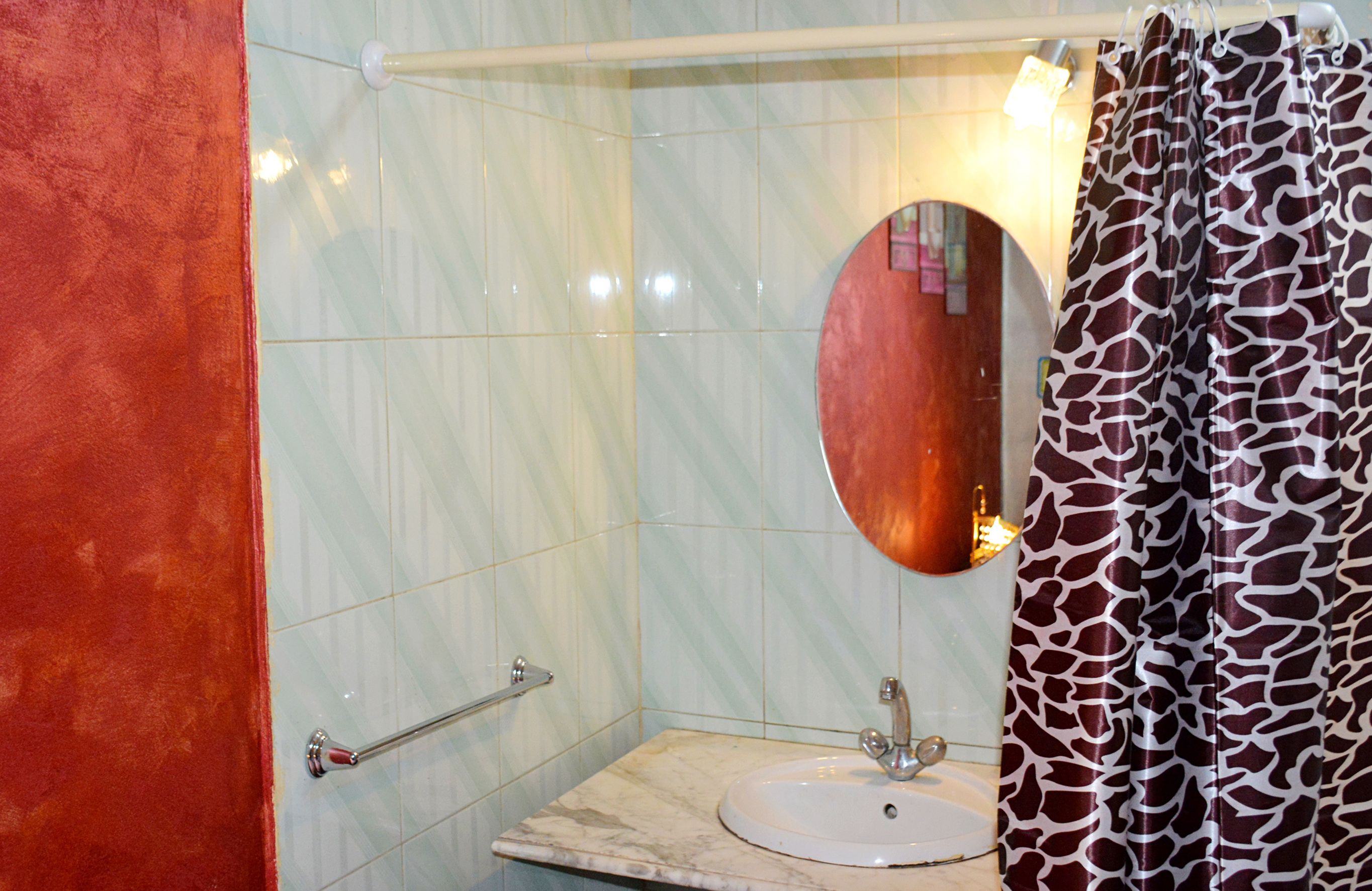 A bathroom with a marble sink, a round mirror, a towel rack, and a giraffe-patterned shower curtain.