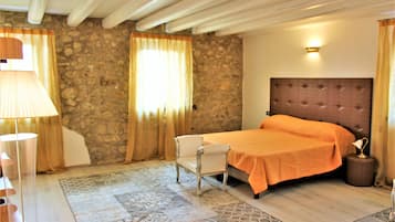 Une chambre avec un mur en pierre, un lit recouvert d’une couverture orange, une chaise blanche, une lampe et une table de chevet avec une lampe.