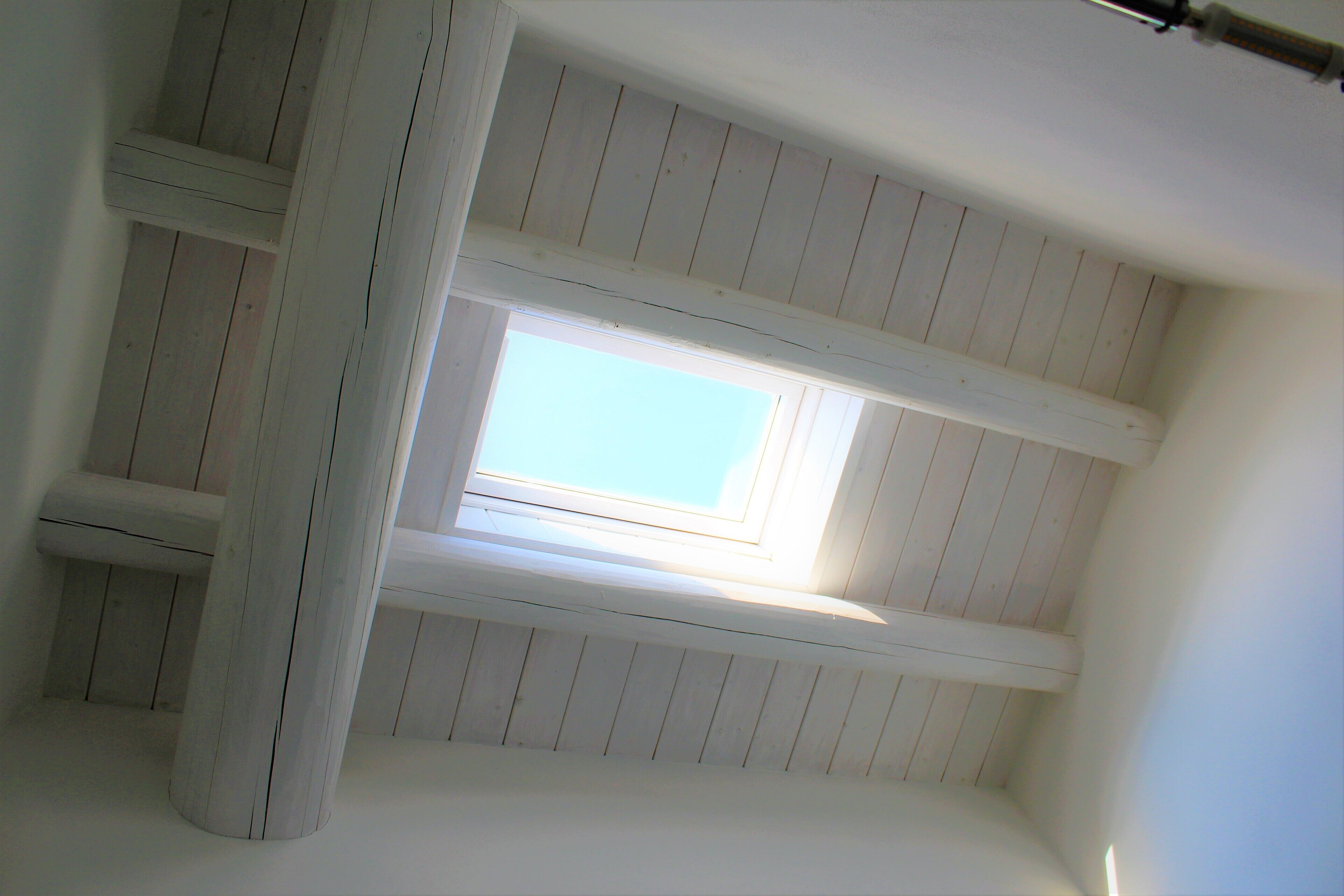 A room with a skylight, wooden beams, and a white ceiling.