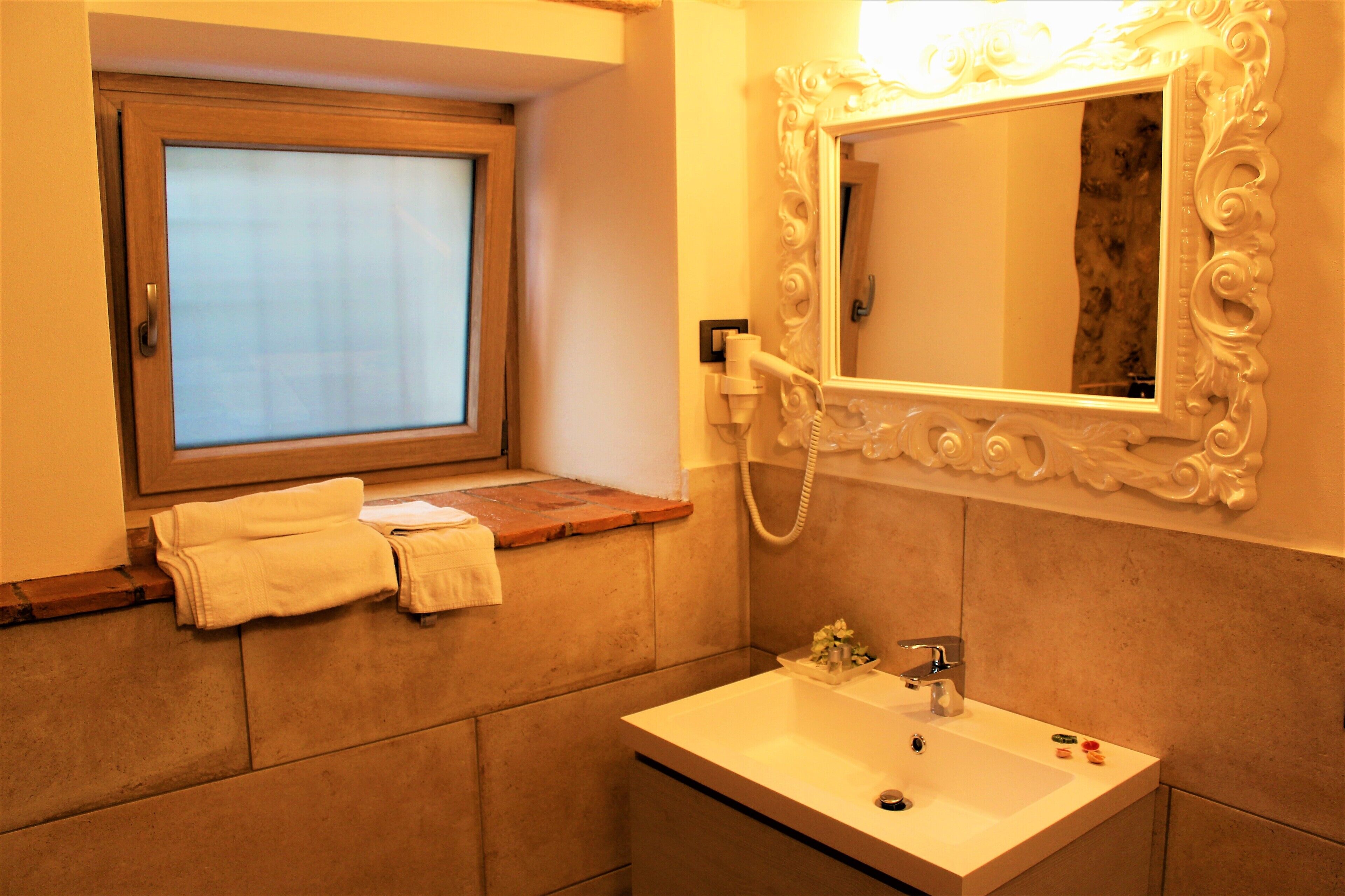 Un baño con ventana, lavamanos y espejo con marco decorativo.