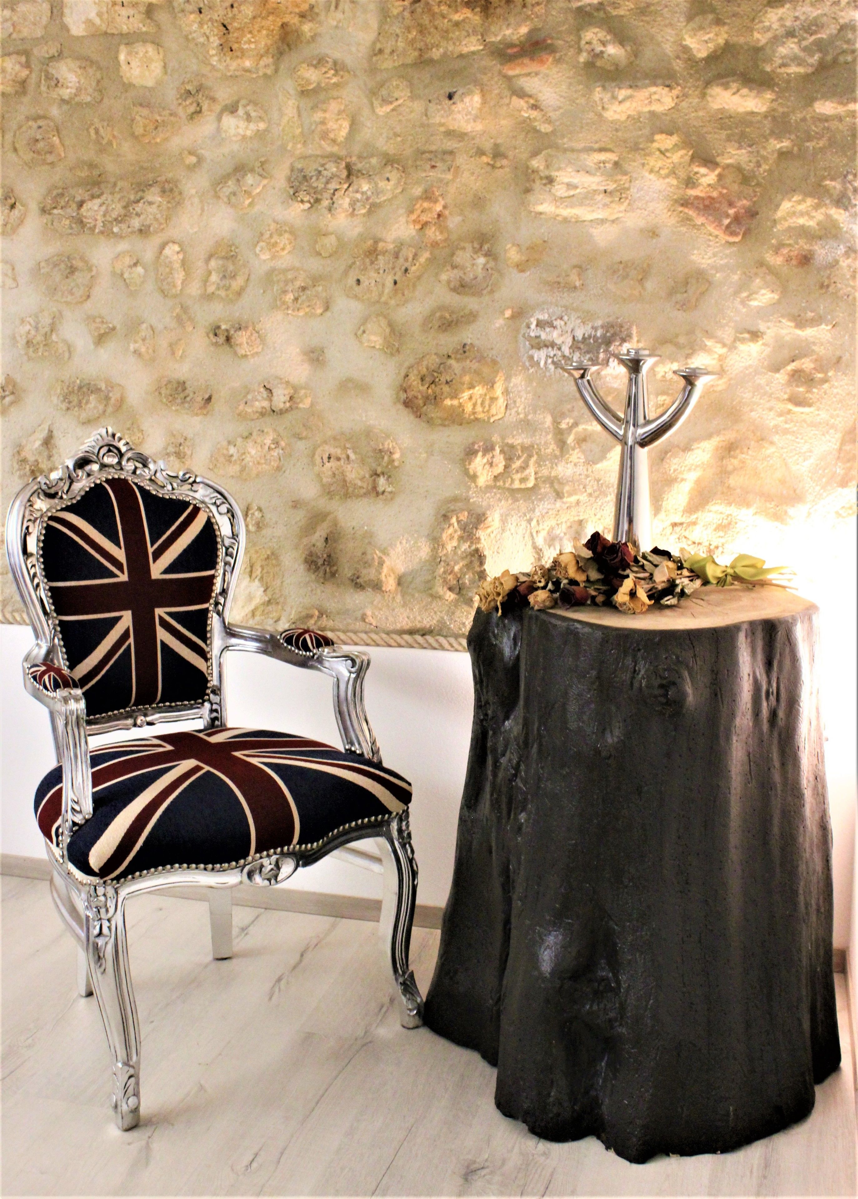 Una silla con diseño de la bandera Union Jack, un candelabro de metal y una mesa hecha con un tocón de árbol.
