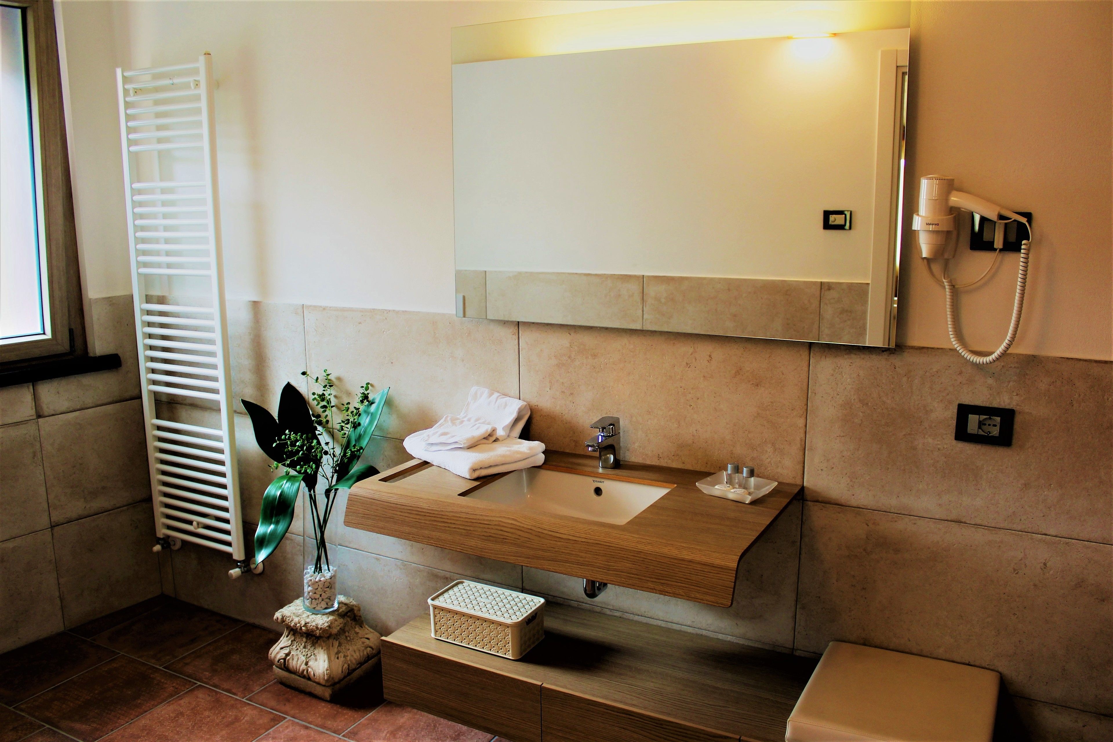 Une salle de bain avec un meuble-lavabo en bois, un évier, un miroir, un porte-serviettes, un sèche-cheveux et un radiateur.