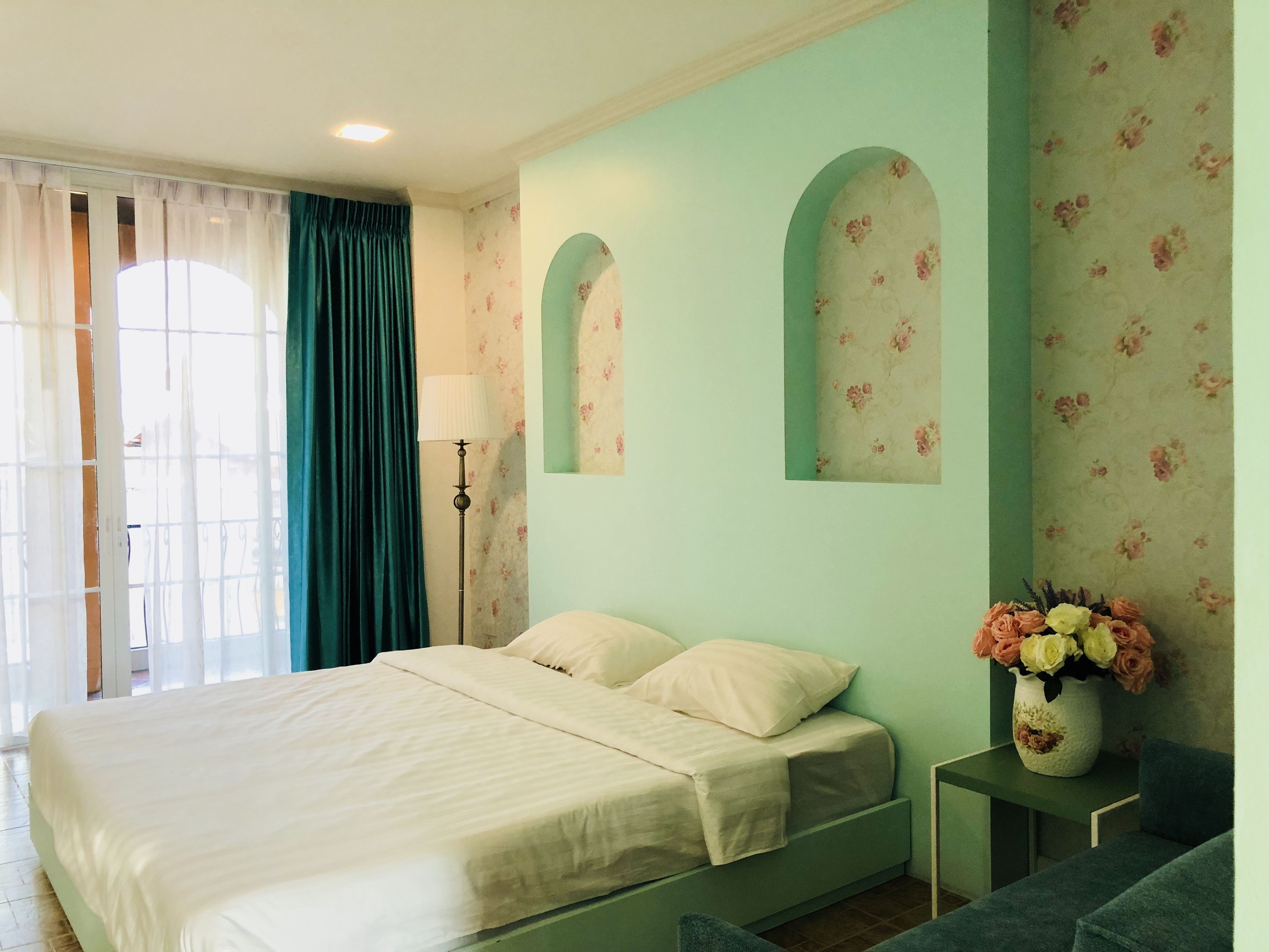Un dormitorio con una cama, una mesita de noche, una lámpara y un florero con flores.