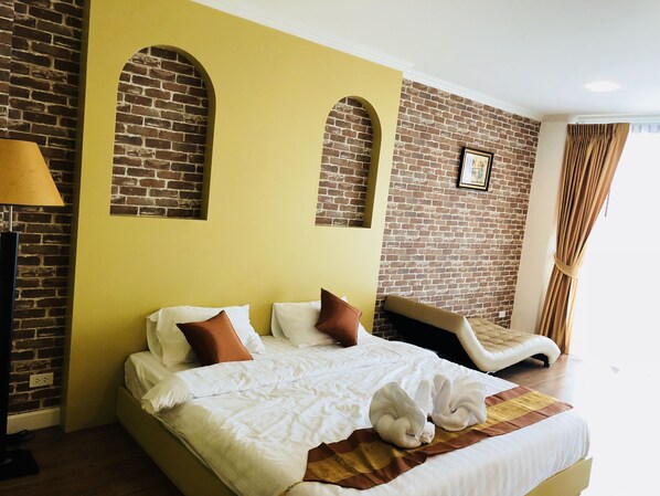 A hotel room with a brick wall, yellow accent wall, a bed with white bedding and brown pillows, a sofa, and a lamp. - Krinnatra Villa (Ban Bueng)