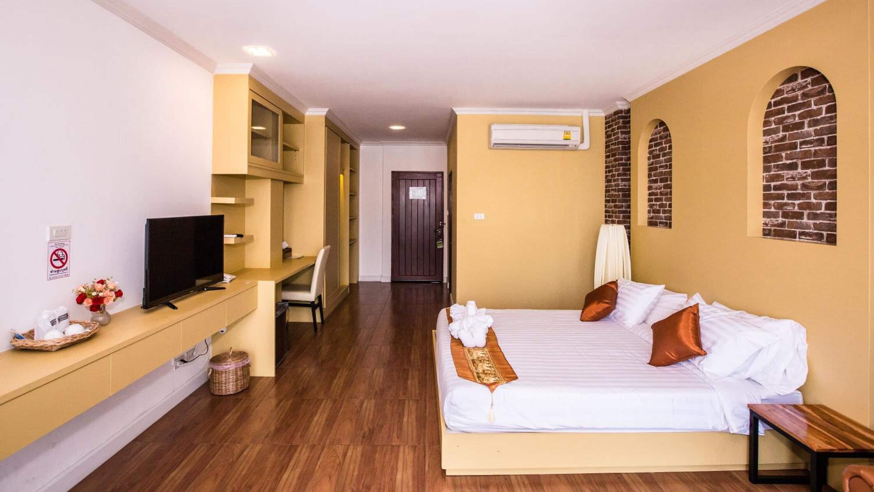 A hotel room with a bed, a desk with a television, a chair, and a small table.