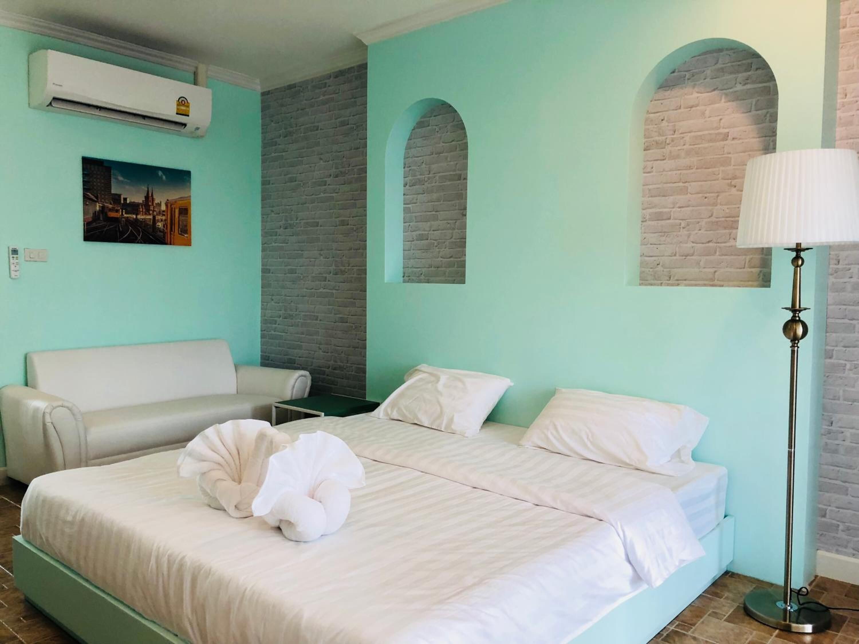 Una habitación de hotel con cama, sofá, aire acondicionado, lámpara y un cuadro en la pared.