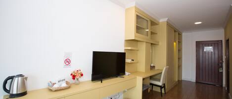 Ein modernes Hotelzimmer mit Flachbildfernseher, Wasserkocher, einem Kosmetika-Set und einem kleinen Tisch mit Stuhl.