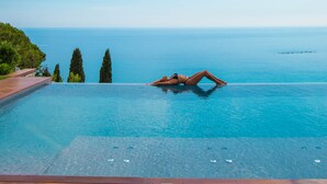 Una persona descansando en la terraza de una piscina con vista al mar.